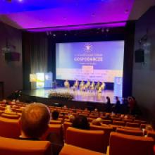 Zdjęcie przedstawia salę kinową w ośrodku kultury z żółtymi fotelami widowni zbiegającymi w dół. W dole sali wielka scena, na której na fotelach siedzą eksperci biorący udział w panelu dyskusyjnym. W tle sceny widać napis IV Dolnośląskie Forum Gospodarcze 19 marca 2026 Oleśnica.